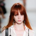Red hair: Model on runway with fiery auburn straight hair with long fringe bangs wearing a white blouse.
