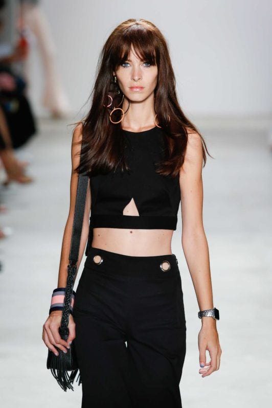 Brunette model on runway with long hair and split bardot bangs wearing all black outfit.