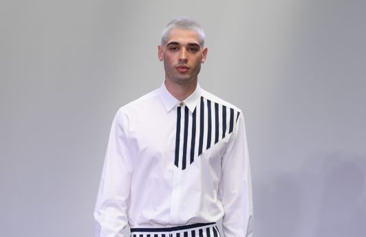 Men's hairstyles 2018: Male on runway with platinum blonde buzzcut wearing a monochrome stripe shirt and trousers.
