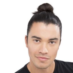 Man bun: Male model with straight dark brown hair in high bun wearing a black tshirt.