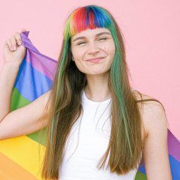 Pride: woman with rainbow fringe and long brown hair holding a pride flag