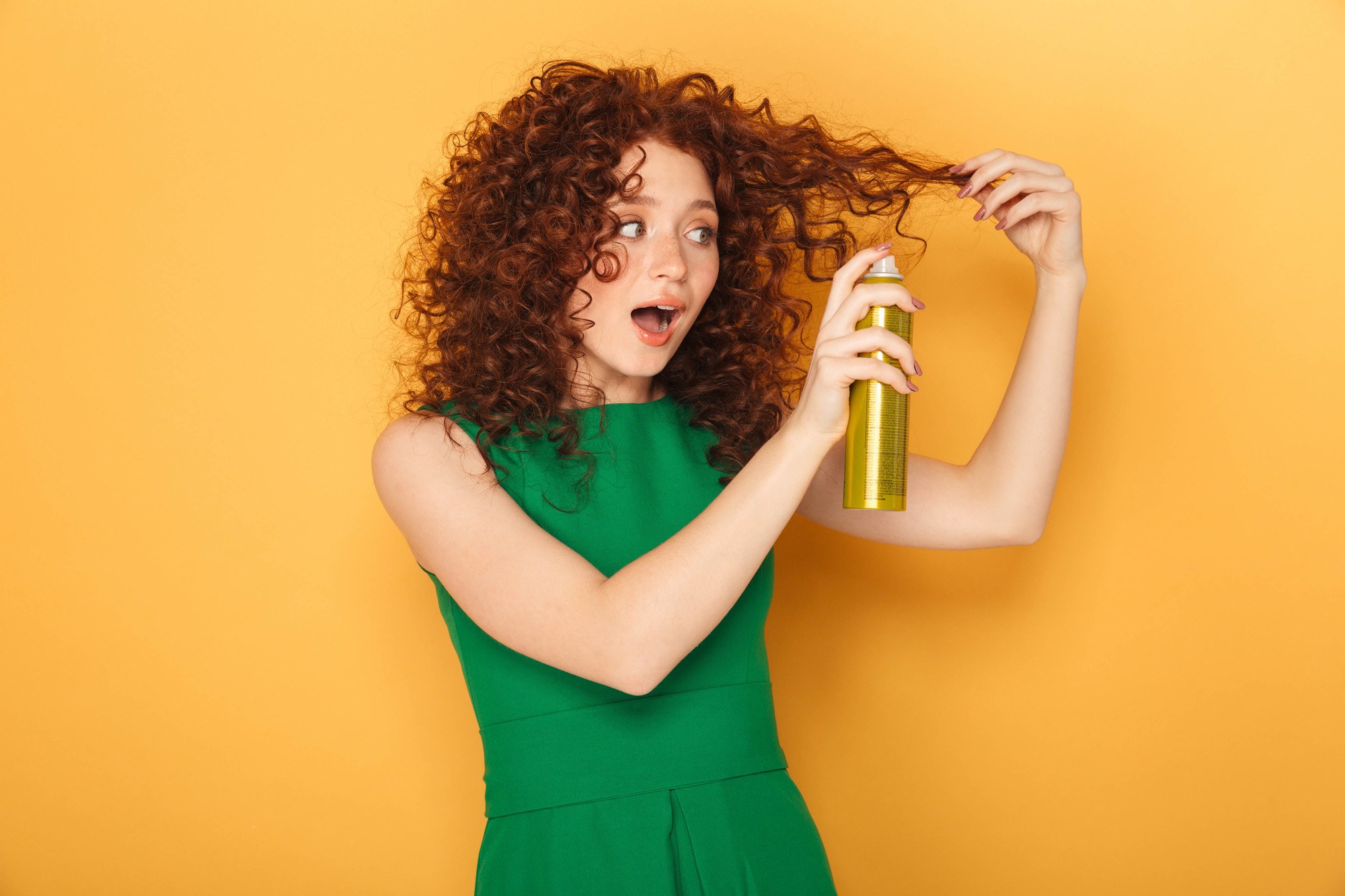 woman with curly red hair spraying product onto her hair