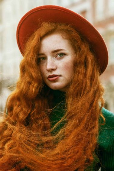 woman with long wavy red hair wearing a hat