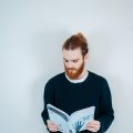 Man with ginger hair wearing a man bun and holding a book