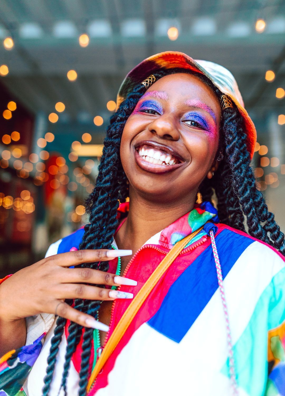 woman with bright, colourful makeup and a multicoloured bucket hat, with her hair in thick, long twists