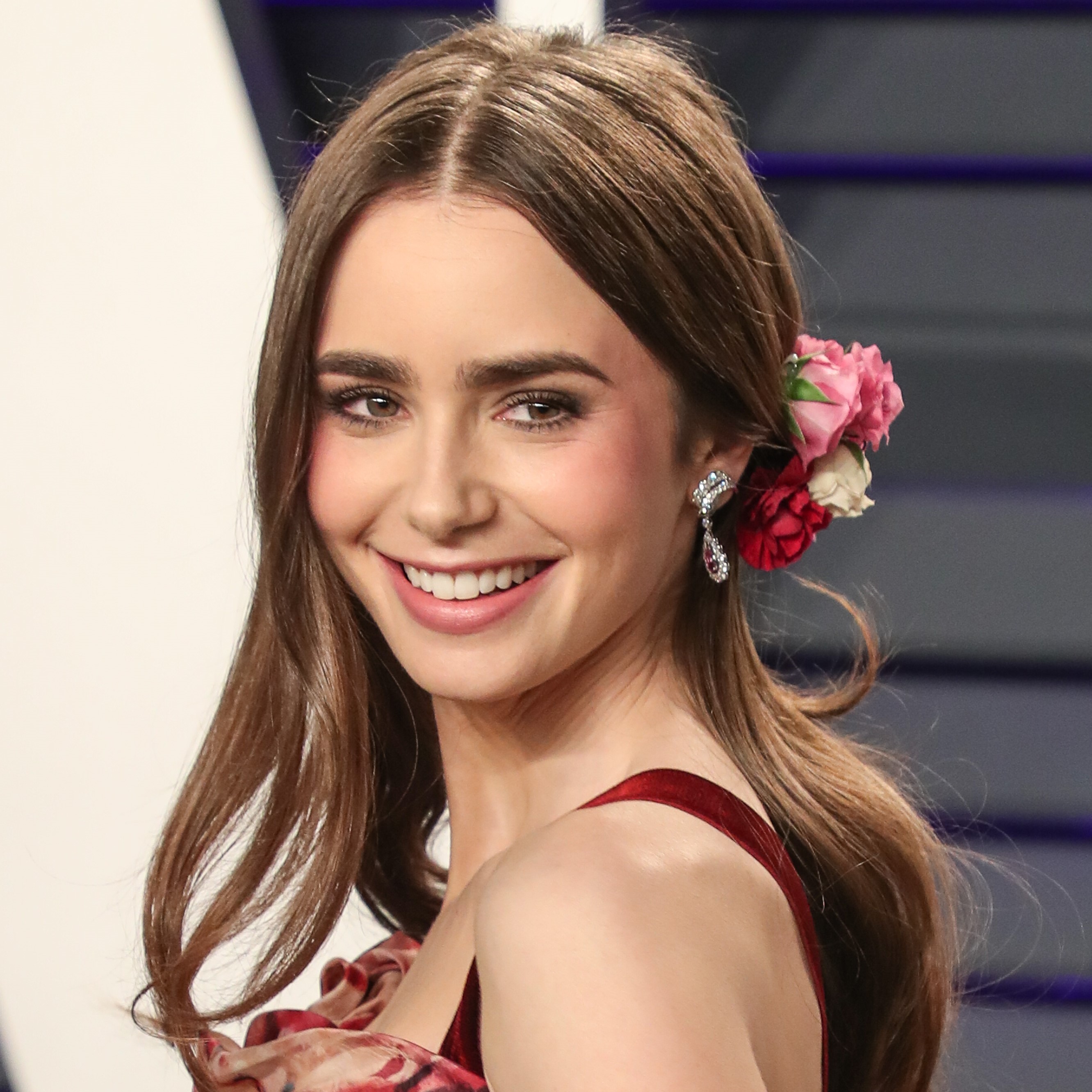 Lily Collins con peinado semirecogido de lado y flores en el cabello