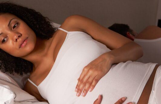 Mujer embarazada con cabello rizado negro, acostada en la cama