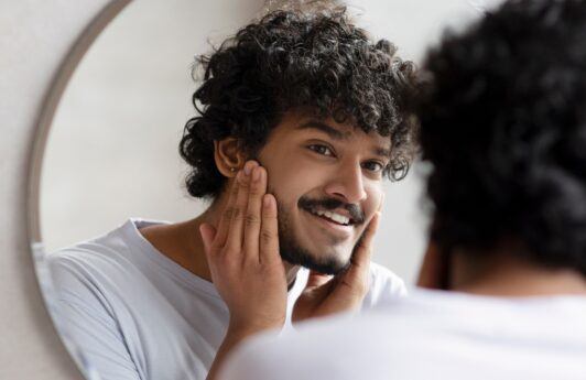 Hombre cuidándose la barba frente al espejo