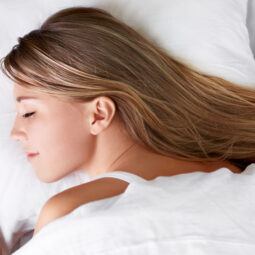 Mujer que duerme con el cabello mojado sobre una cama blanca