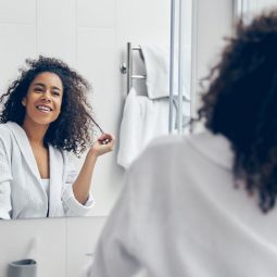 mulher com cabelo cacheado s olhando no espelho do banheiro tocando os fios