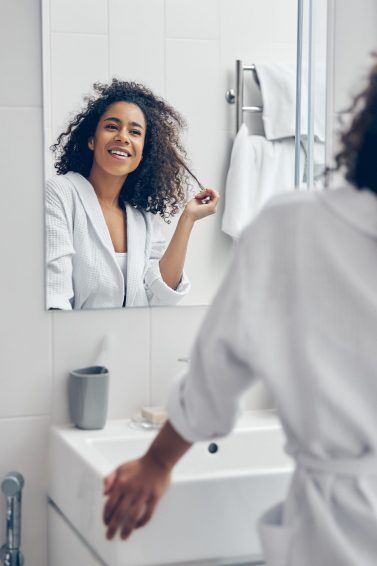 mulher com cabelo cacheado s olhando no espelho do banheiro tocando os fios