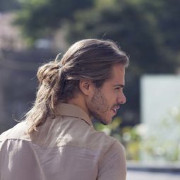 Homem posa com coque masculino baixo, ao ar livre, mostra resultado do penteado