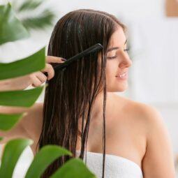Mulher de cabelo castanho molhado fazendo detox capilar no cabelo com algumas plantas no banheiro