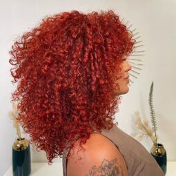 Influenciadora digital com cabelo ruivo vermelho cacheado com franja posando de perfil