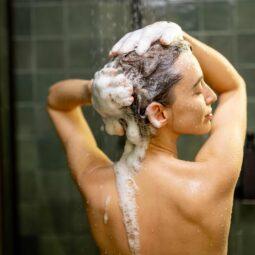 mulher de costas lavando os cabelos com shampoo