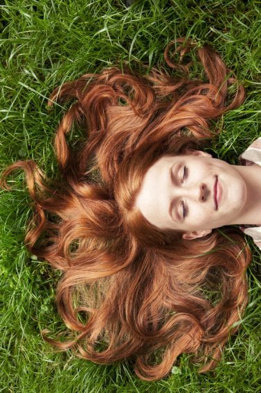 mulher ruiva deitada com os cabelos espalhados na grama
