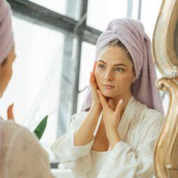 mulher com toalha na cabeça se olhando no espelho