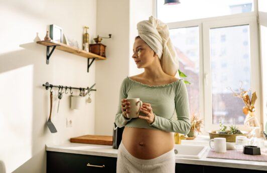 mulher grávida segurando xícara com toalha na cabeça
