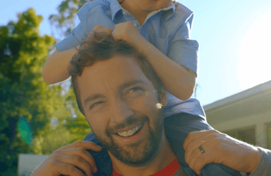 a bearded man standing outside playing with a kid