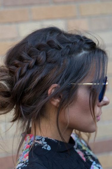 a side view of a woman with simple updos with a bun standing next to a brick wall