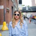 a blonde woman walking on the street in the city wearing sunglasses and a blue striped shirt