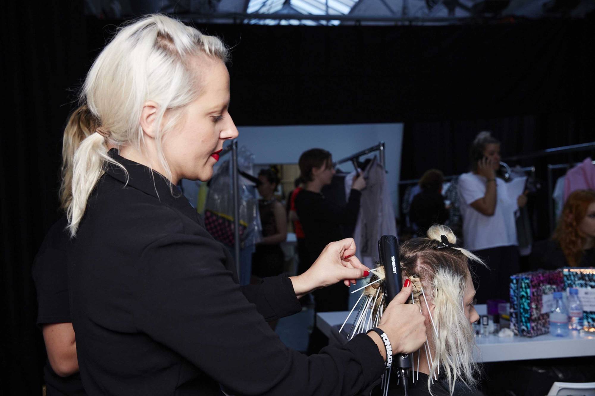 hair stylist using straightener to create styles backstage at London fashion week