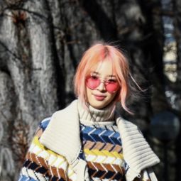 a woman standing outside wearing colorful coat with peach hair long bangs