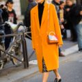 a short-straight blonde hair woman walking down the street wearing a bright yellow coat and an animal print dress