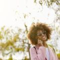 an afro woman wearing sunglasses calling someone while standing outside