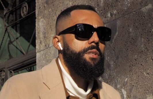 Man with a high taper fade haircut and a beard wearing sunglasses outdoors