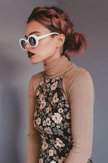 side view of woman with short metallic pink red hair styled with a headband braid secured into a side bun
