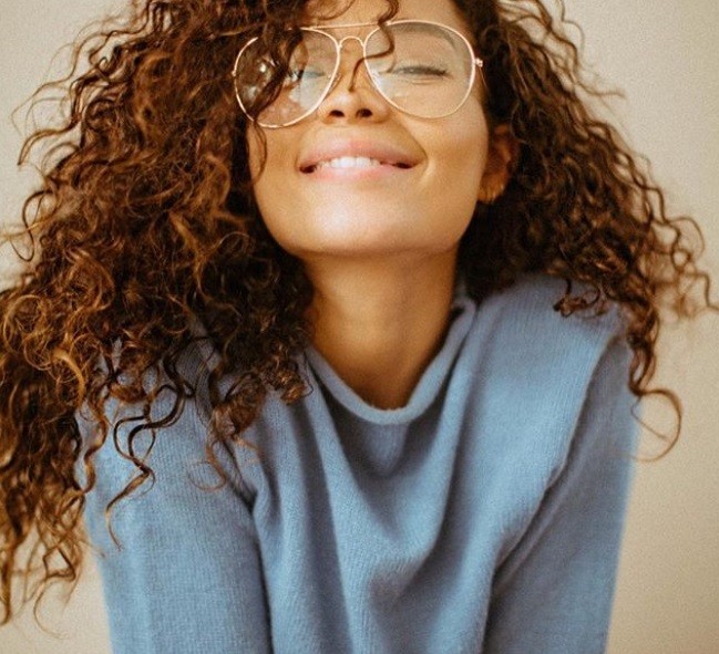 Food for healthy hair guide: Woman with healthy long natural curly hair, wearing a blue jumper and smiling