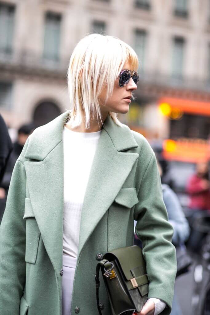 side view of a woman with white hair, a green coat and sunglasses