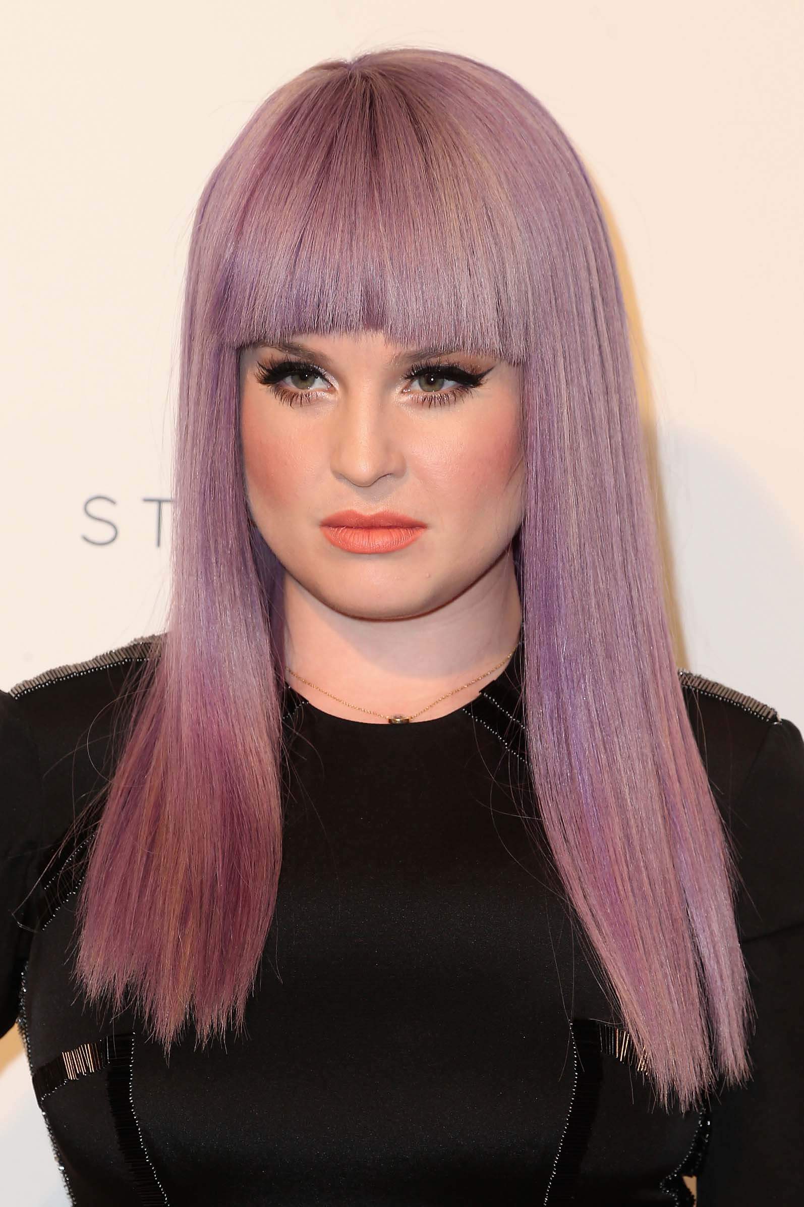 close up shot of kelly osbourne with purple hair with blunt bangs, wearing all black on the red carpet