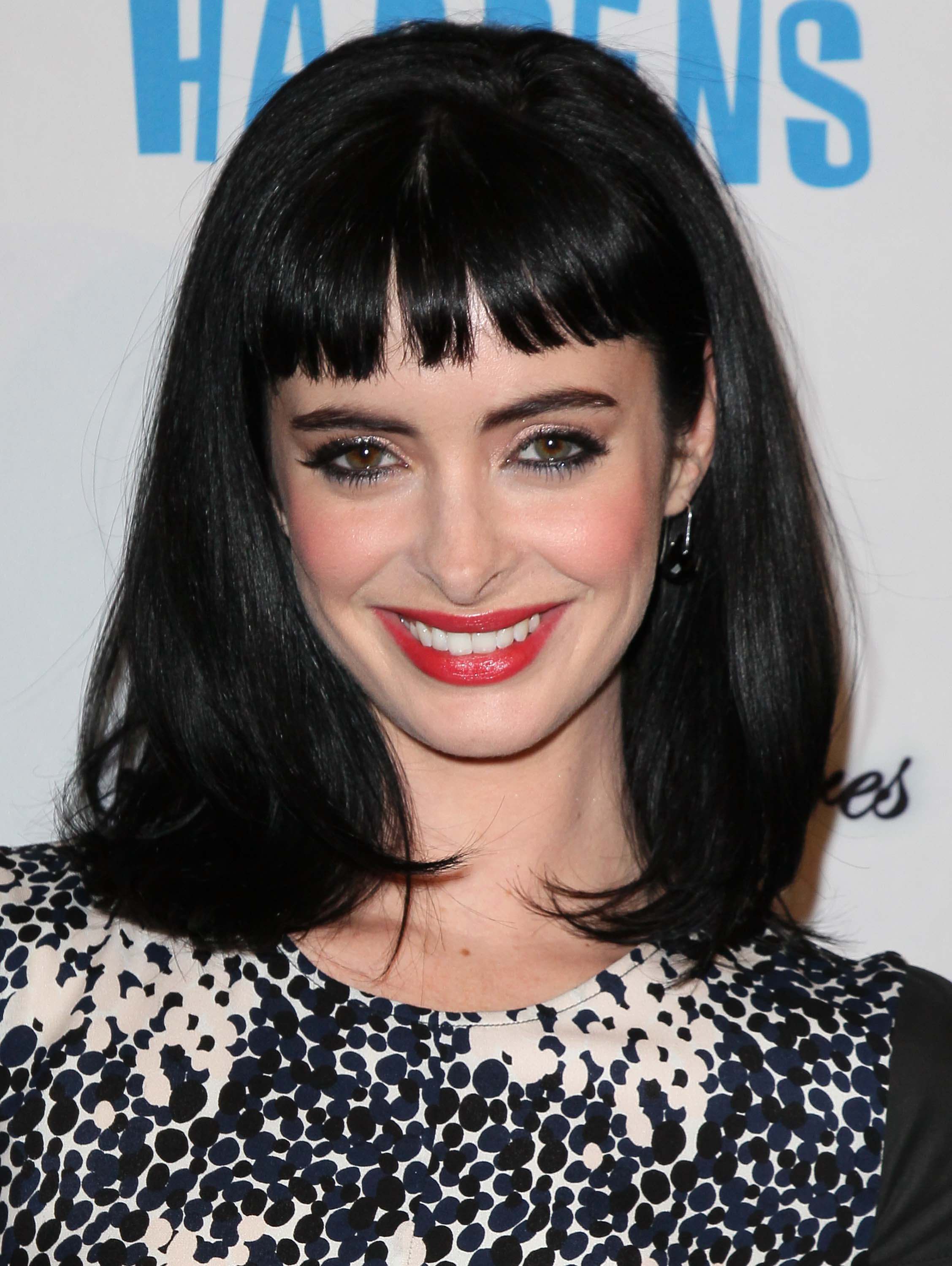 close up shot of Krysten Ritter with bettie page-inspired fringe hairstyle, wearing blue and black dress and posing on the red carpet