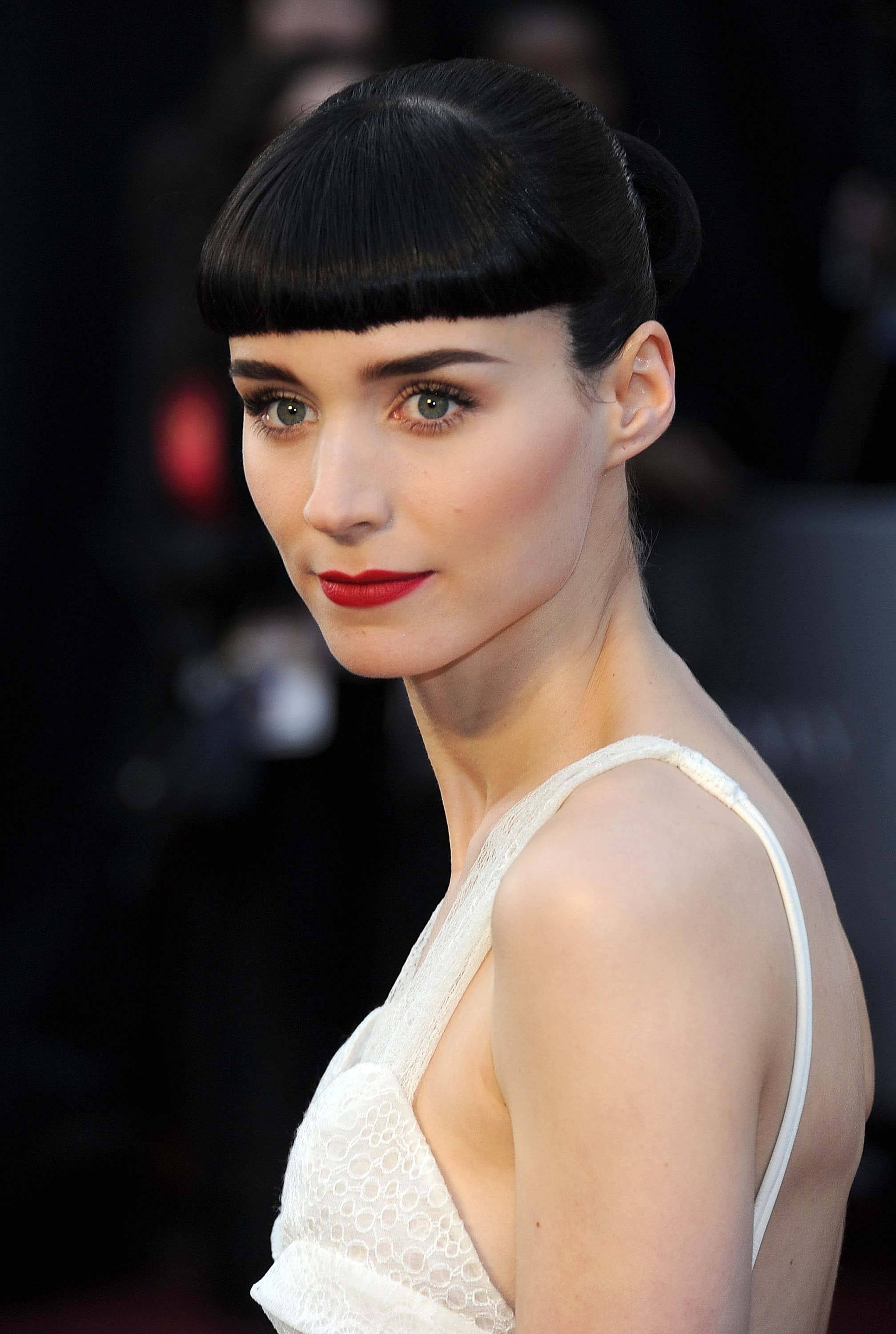 close up shot of rooney mara with blunt bangs and bun hairstyle, wearing red lipstick and white dress on the red carpet