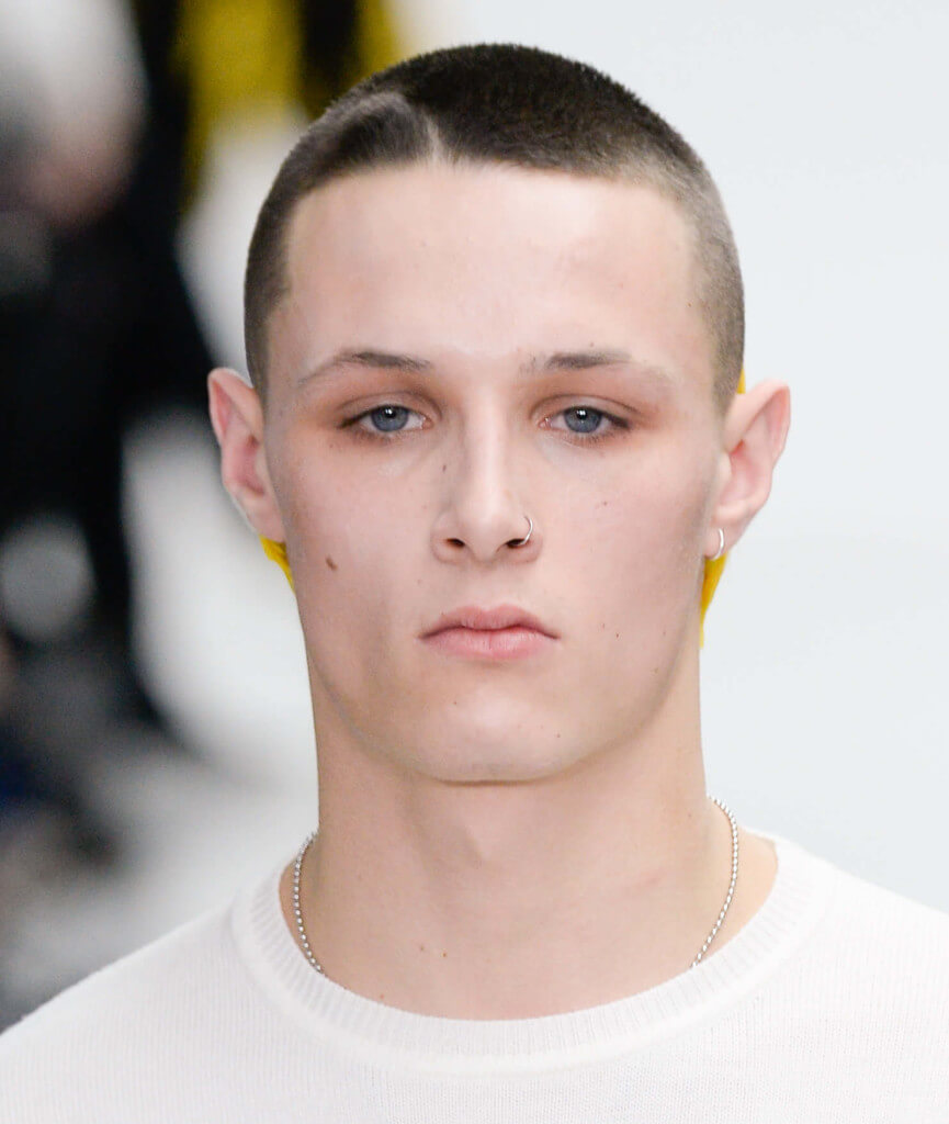 male model on the runway wearing a white top with his brown hair in a buzz cut style