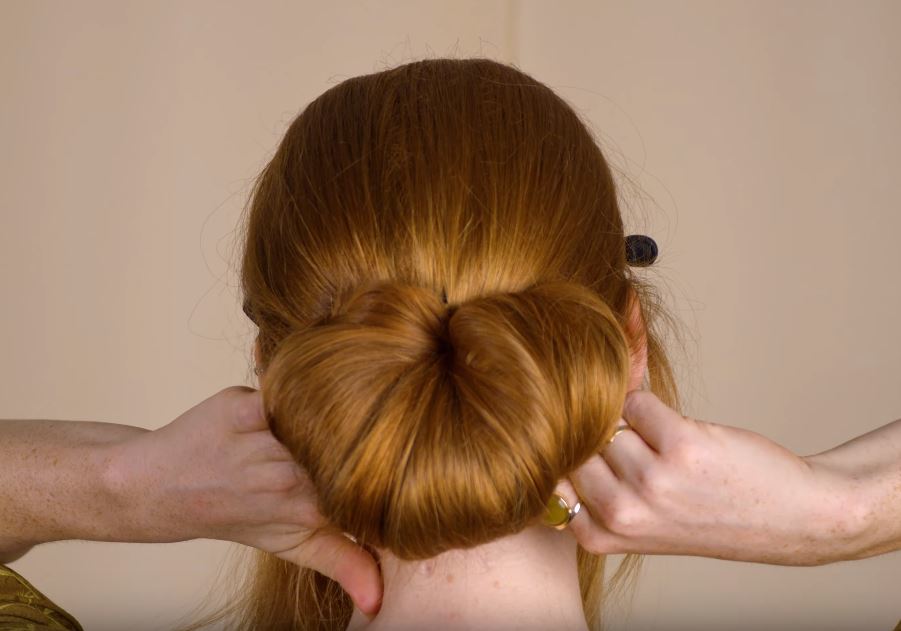 The back of a red haired woman pinning a chignon bun