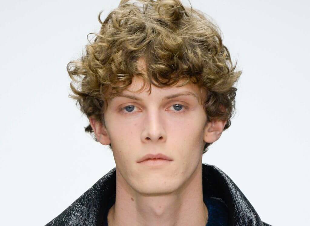 male model on the runway with his dirty blonde curly hair worn in a frontal fringe