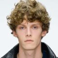 male model on the runway with his dirty blonde curly hair worn in a frontal fringe