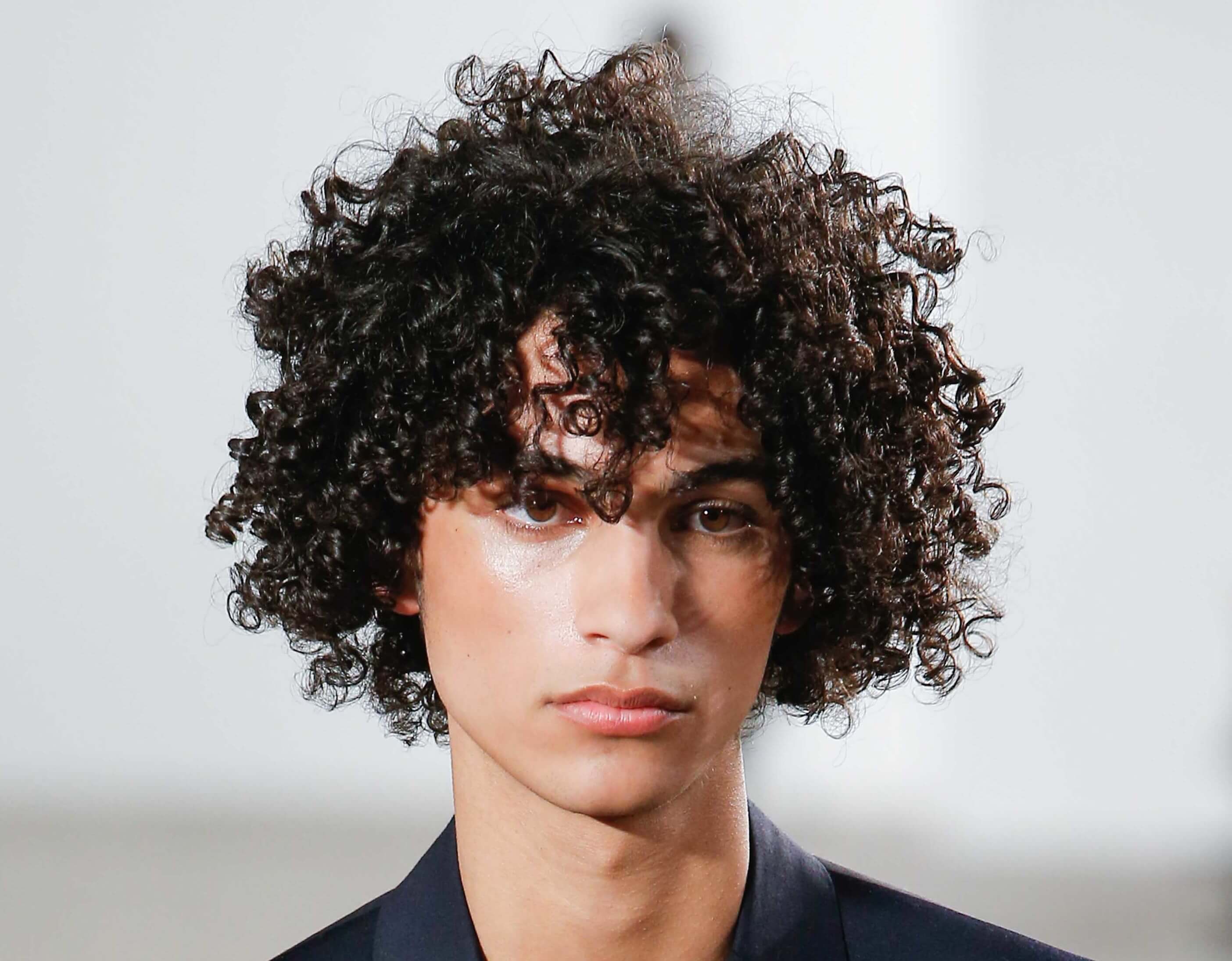 male model on the runway with dark brown curly hair worn long and loose