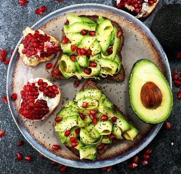 Food for healthy hair guide: Flat lay shot of avocado toast with pomegranate seeds scattered around