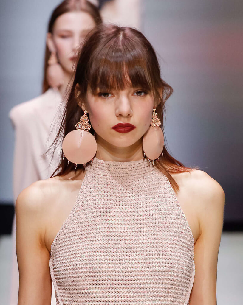 woman on the runway with a long fringe hairstyle wearing a pastel pink outfit