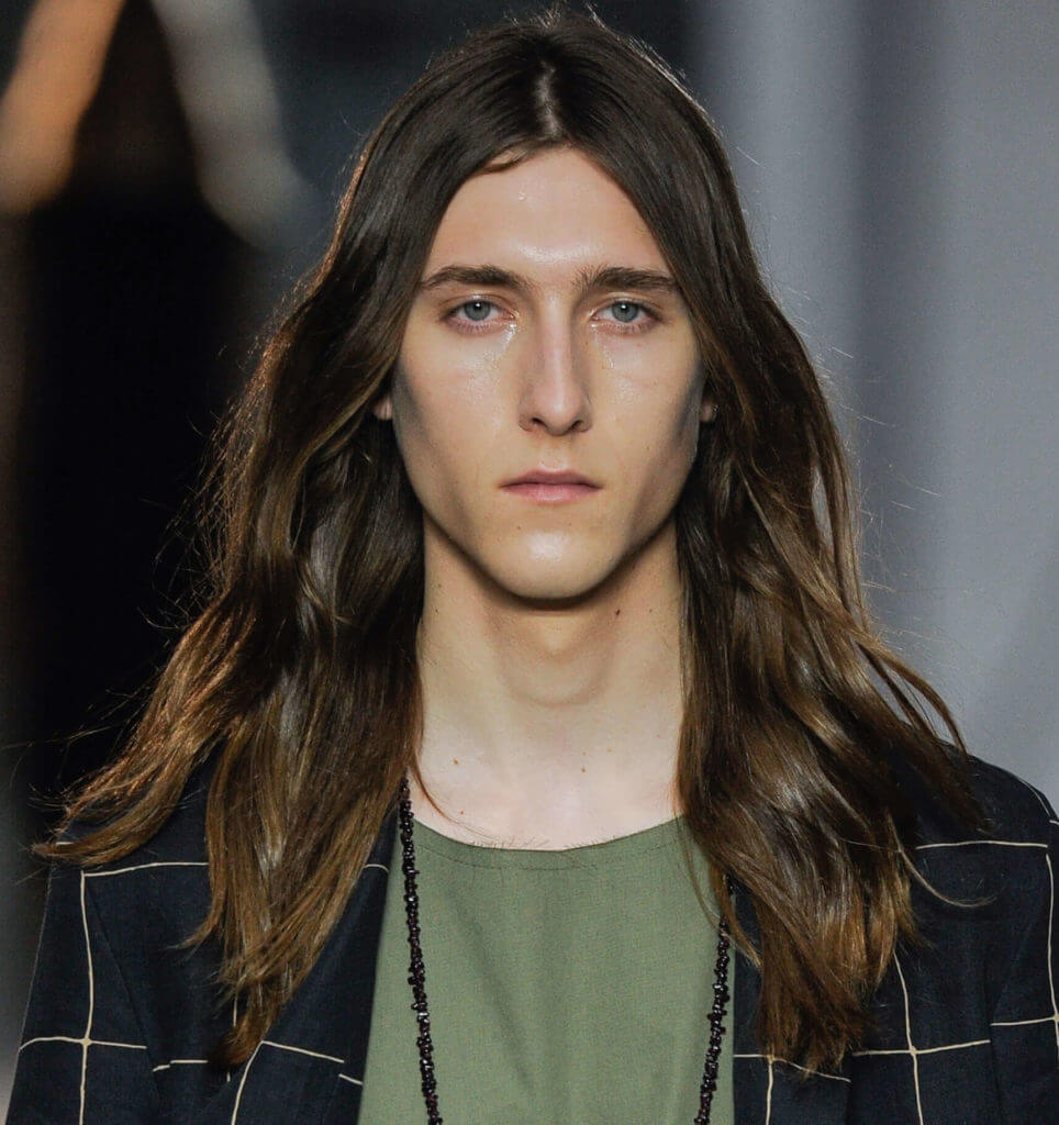 male model on the runway wearing a navy blazer and a green tshirt with his long brown wavy hair worn down
