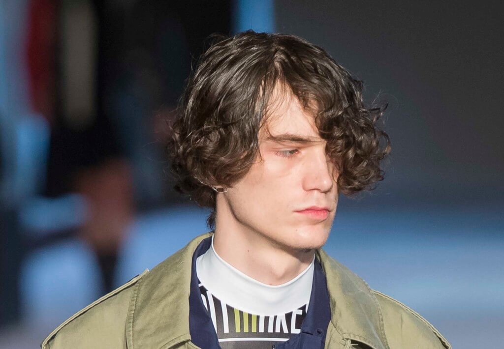 male model on the runway with his dark hair curly hair worn in a side fringe