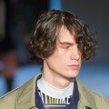 male model on the runway with his dark hair curly hair worn in a side fringe