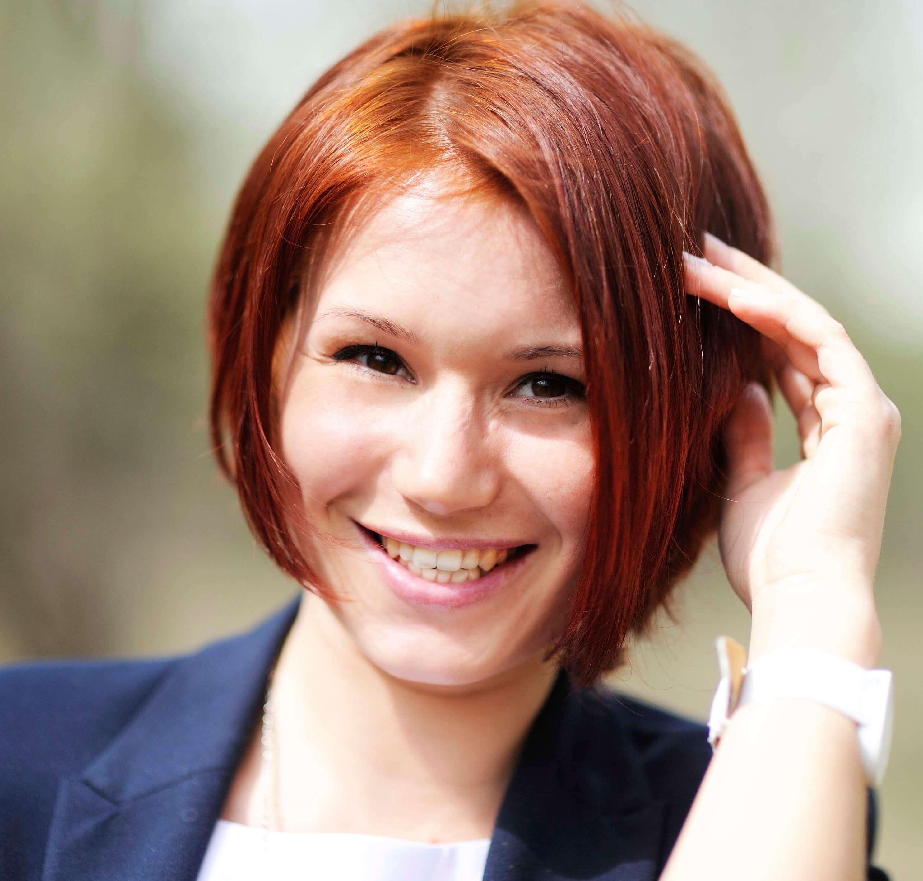 Red haired woman with an angled bob haircut, touching her hair with her hands.