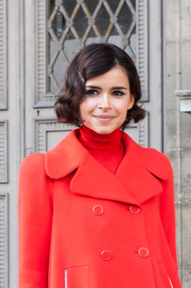 a short hair girl smiling outside while wearing red coat