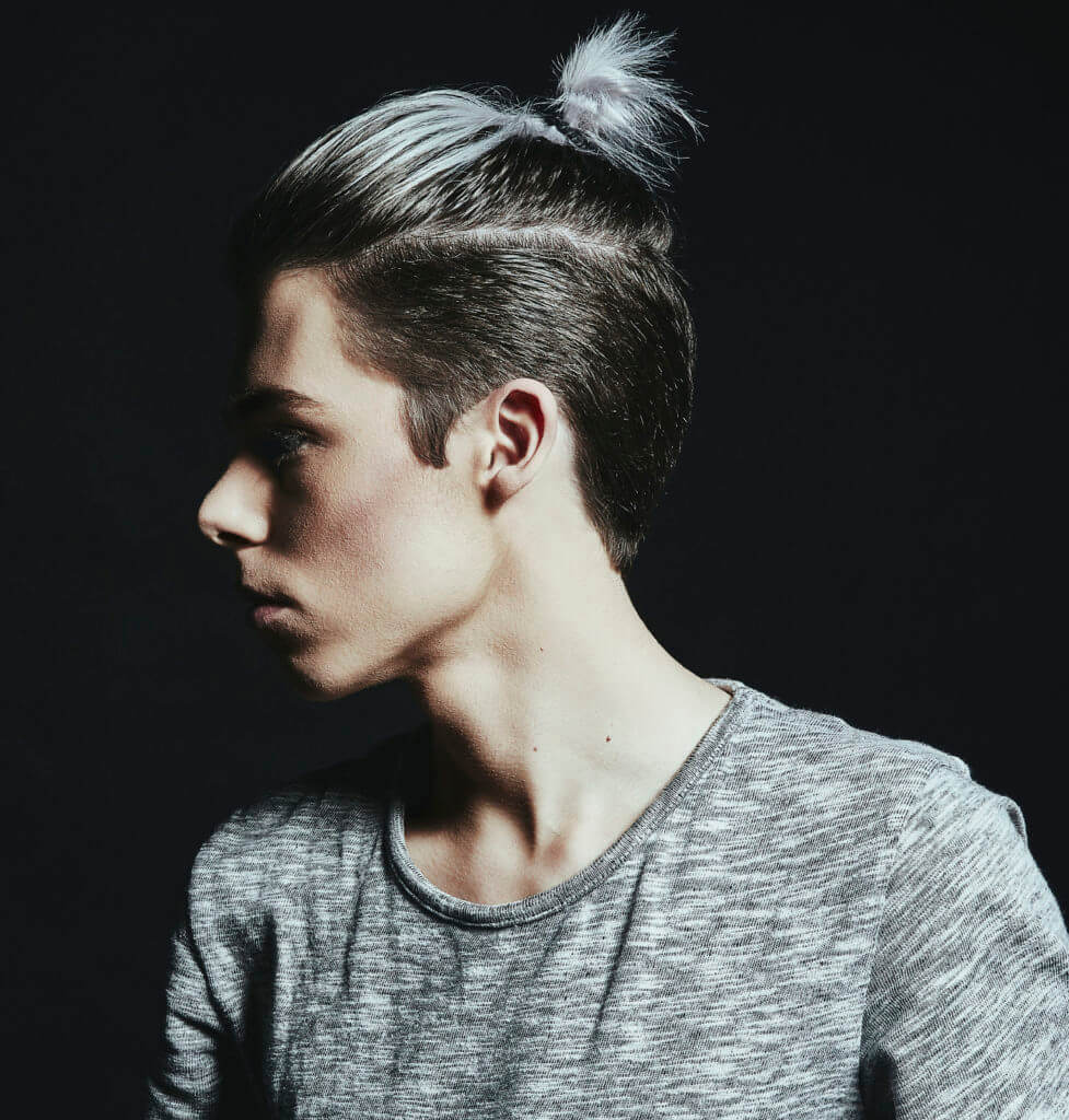 side view of a man wearing a grey top with his hair worn in a man bun with am undercut