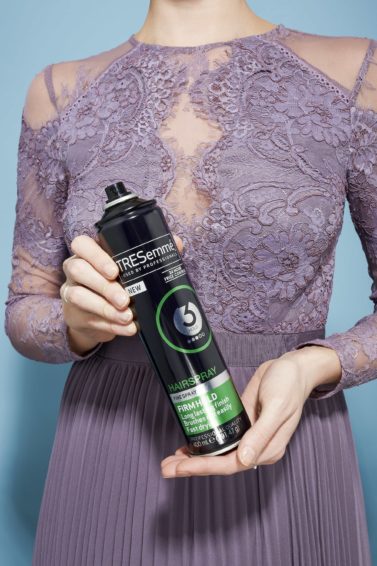 Hairspray guide: Woman holding TRESemme hairspray in her hands wearing a pale purple lace dress.